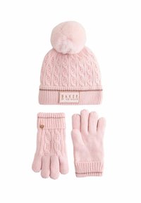 Hellrosa Strickmütze mit Pompon, Kabelmuster und einem dekorativen Etikett. Passende hellrosa gestrickte Handschuhe mit strukturiertem Design.