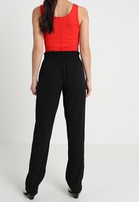 Röd ärmlös topp som matchas med högmidjade svarta byxor. Byxorna har en elastisk midja och är tillverkade av ett lätt tyg.