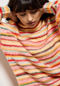 Sweter dzianinowy w wielokolorowe paski w odcieniach różu, pomarańczy, czerwieni i zieleni. Okrągły dekolt z widocznymi teksturowanymi ściegami.