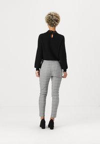 Black knit sweater with a lace collar, paired with gray plaid fitted pants and black block-heeled shoes. View from the back.