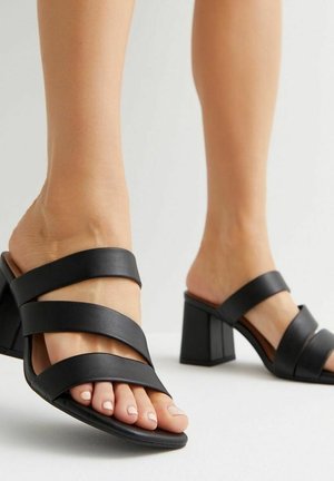 Czarne sandały na obcasie z szerokimi paskami ze skóry, odkrytymi palcami i blokowym obcasem. Gładka tekstura i minimalistyczny design.