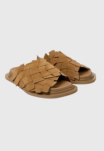 Sandalias de ante marrón con tiras anchas y trenzadas, y suelas planas en capas sobre un fondo liso.