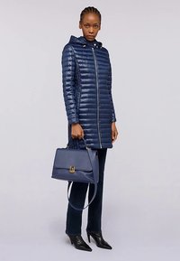 Piumino navy con cappuccio, design trapuntato orizzontale e cerniera frontale. Abbinato a una borsa blu scuro con chiusura dorata e tracolla lunga.