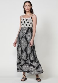 Robe maxi avec une jupe à motifs noir et blanc, un corsage texturé de couleur claire et des bretelles fines ; silhouette fluide.