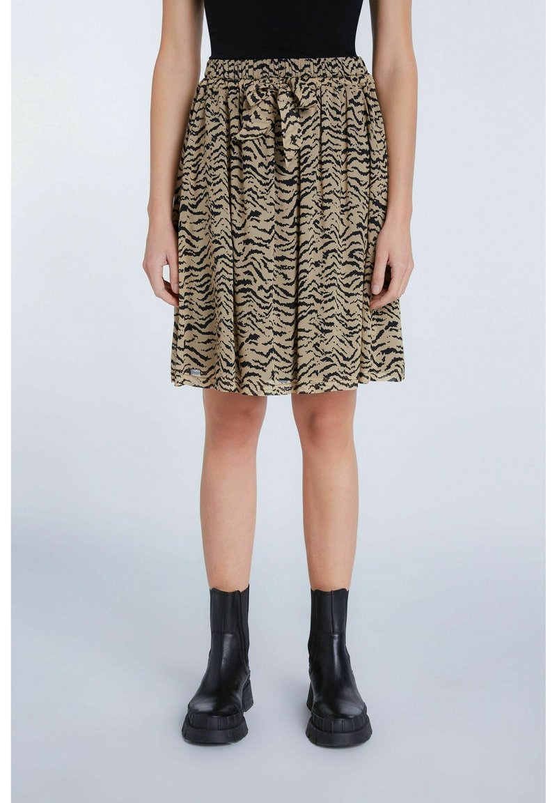 Jupe rayée brun et noir à motifs de tigre avec une ceinture élastique et un détail noué. Associée à des bottines noires.