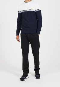 Granatowy sweter robiony na drutach w biało-niebieskie poziome paski, z żółtym logo. Połączony z czarnymi spodniami i czarnymi sneakersami.