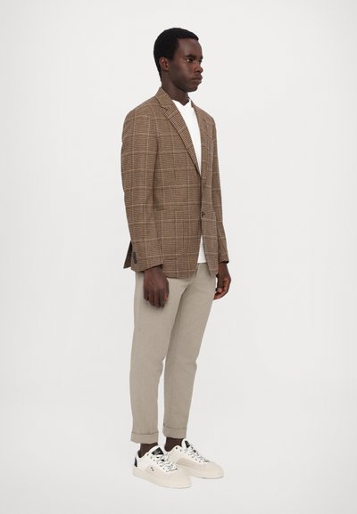 Brown plaid blazer with a fitted design, paired with light beige trousers and white sneakers, featuring black accents on the shoes.