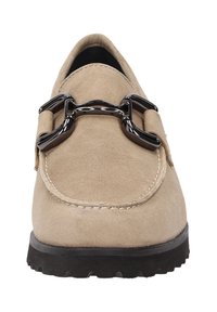 Mocassin en daim beige avec un bout rond, présentant un accent métallique noir sur le dessus et une semelle en caoutchouc noir texturé.
