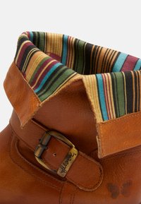 Braune Leder-Ankle-Boots mit umgeschlagenem Kragen und buntem gestreiftem Stoff. Metall-Schnallen-Detail am Riemen, strukturierte Oberfläche.
