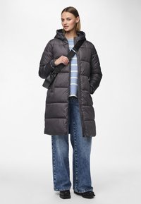 Grå pufferjakke med hette, glidelås foran og kviltet design. Båret over en lys blåstripet genser og kombinert med vide denimjeans.