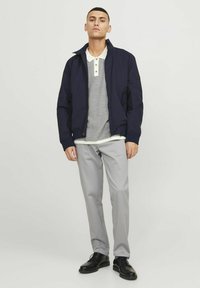 Chaqueta de bombardero marina, polo a rayas gris con cuello crema, pantalones gris claro, zapatos negros. Enfoque en líneas limpias y ajuste contemporáneo.