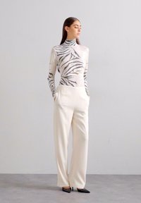 Dugi rukavi, visokog vrata, s uzorkom zebra u bijeloj i crnoj boji; kombiniran s širokim krem hlačama i crnim cipelama s izrazito špicastim vrhom.
