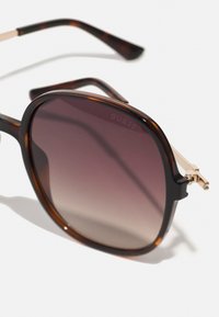 Solbriller med tortoise-farget ramme, brune gradientlinser og gullmetalldetaljer på stengene. Firkantet form med blank finish.