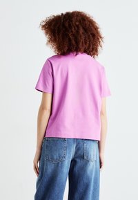 T-shirt cropped a maniche corte in cotone rosa acceso. Presenta una scollatura rotonda e una vestibilità comoda, abbinato a jeans di jeans a vita alta.