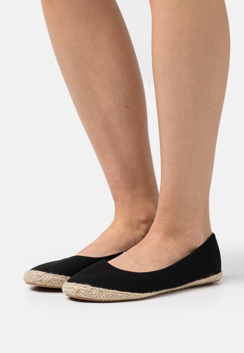 Ballerines en toile noire avec un bout arrondi et des détails en corde de jute le long de la semelle. Le design est minimaliste et présente une texture lisse.