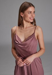 Cowl neck dress in muted mauve satin fabric, featuring thin straps, a belt at the waist, and a relaxed fit with subtle pleats.