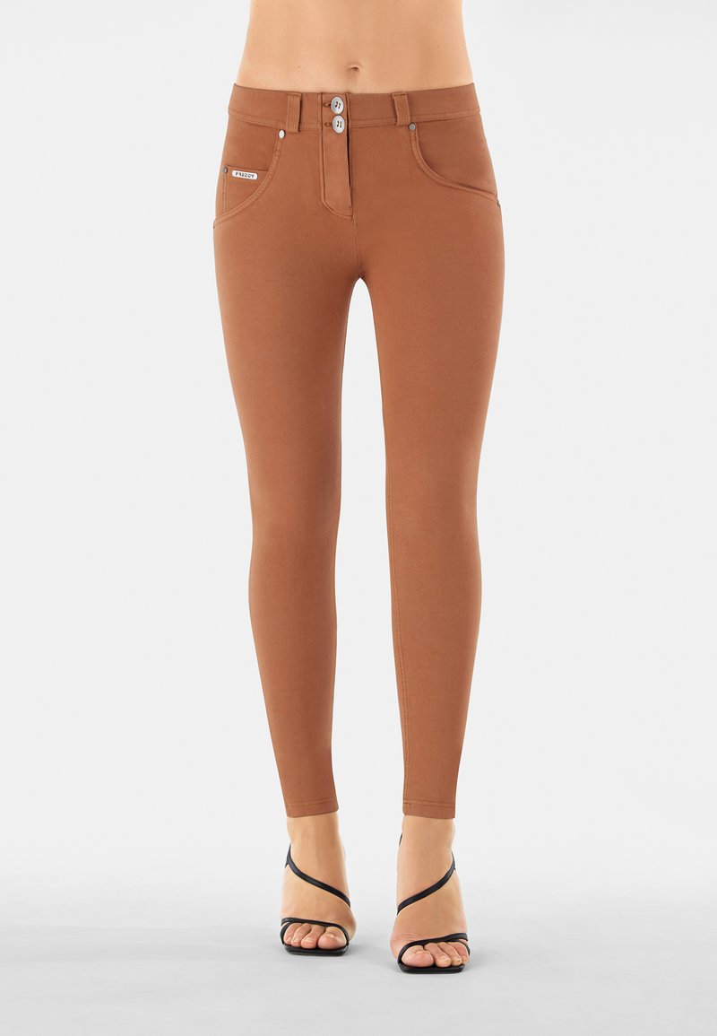 Leggings marroni con una texture liscia, design a vita alta, chiusura con doppio bottone e tasche anteriori, abbinati a tacchi neri con fasce.