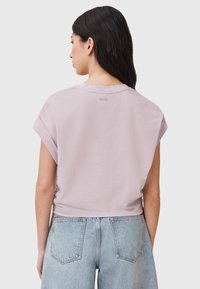 T-shirt a maniche corte e cropped in tessuto lilla chiaro; presenta un'etichetta discreta sul retro e maniche arrotolate, abbinato a pantaloni shorts in denim a vita alta.