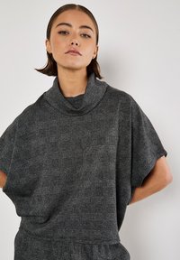 Cowl-neck topp i ett strukturerat svart och grått rutmönster med korta ärmar och lös passform, tillverkad av mjukt tyg.