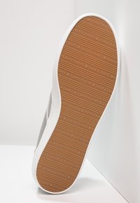 Baskets grises avec bordure en caoutchouc blanche et semelle texturée marron, arborant la marque "JACK & JONES" embossée en motif répétitif.