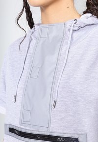Light gray hoodie with a soft fabric, featuring a contrasting gray panel, drawstrings, and a zippered pocket at the front.