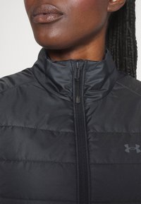 Mustapuffatakki, jossa on korkea kaulus, edessä vetoketju ja pieni brändilogo. Materiaali on sileä ja jonka pinnassa on tikattu rakenne.