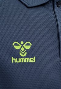 Polo shirt navy à tissu texturé, avec un logo vert vif et le texte "hummel" affiché en évidence sur le côté gauche.