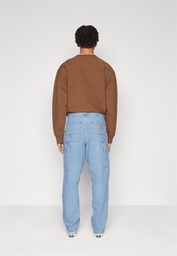 Brauner Sweatshirt mit Rundhalsausschnitt, kombiniert mit hellblauen Cargo-Hosen, die mehrere Taschen und einen Logopatch auf der Rückseite haben.
