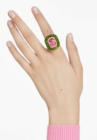 Groene acrylring met een roze rechthoekige edelsteen, omringd door gouden accenten, weergegeven op een hand met een lichte huidskleur.