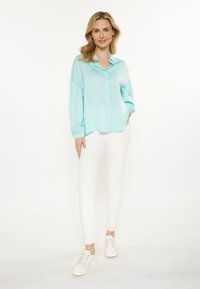 Lichtblauw, knoopsluiting blouse met lange, puffed mouwen; gemaakt van een gladde stof. Gecombineerd met strakke witte broeken en witte sneakers.