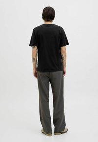 Svart bomullströja med klassisk rund halsringning, i kombination med ljusgrå vida byxor och beige slip-on skor. Bakifrån.