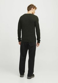 Dunkelgrüner gestrickter Pullover mit einem strukturierten Muster, eng anliegende lange Ärmel und Rundhalsausschnitt, kombiniert mit schwarzen Hosen und Sneakers.