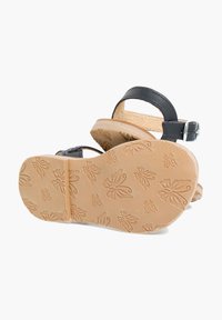 Mustat nahkakengät, joissa on paksu pohja, säädettävä nilkkahihna ja tekstuurinen beige kumipohja, jossa on perhoskuvioita.