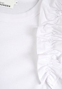 Biely rebrovaný top s nariaseným detailom na ramene, vyrobený z mäkkej tkaniny s hladkou textúrou a klasickým okrúhlym výstrihom.