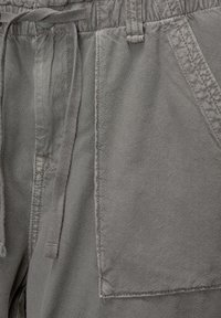 Pantalones de algodón grises con un corte holgado, cintura ajustable con cordones y bolsillos laterales con detalles de costuras visibles.