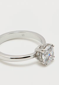 Ασημένιο δαχτυλίδι αρραβώνων με στρογγυλό πολύτιμο λίθο με μπριγιάν κοπή που κρατείται από τέσσερα νύχια σε απλή μπάντα.