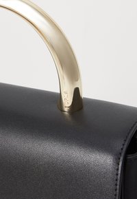Borsa a mano in pelle nera con manico in metallo dorato lucido. La superficie ha una finitura strutturata, con un marchio visibile sul manico.