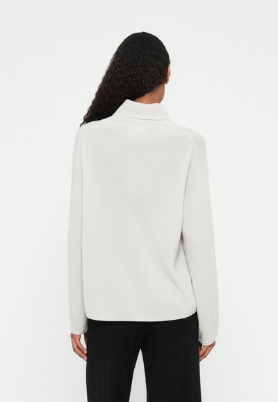 Pull en maille gris clair avec col rabattu et manches longues, présentant une surface texturée et une coupe décontractée.