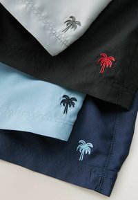 Trois chemises à col en gris clair, noir et bleu clair, ornées de logos de palmier brodés de différentes couleurs sur les poignets.