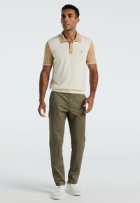 Cremefarbendes und tanfarbenes kurzärmliges Poloshirt mit Kragen, kombiniert mit olivgrünen Cargo-Hosen und weißen Sneakers. Einfaches Design ohne Muster.