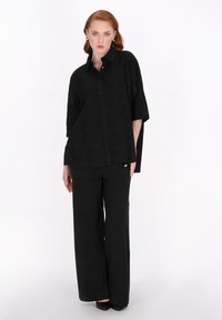 Schwarze bestickte Bluse mit Kragen und kurzen Ärmeln, kombiniert mit weit geschnittenen schwarzen Hosen. Glattes Stoff mit strukturierten Details.