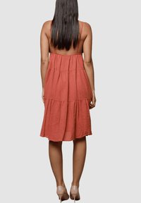 Vestido sin mangas de color naranja oxidado con un diseño de capas y un corte en la espalda, hecho de tela ligera, que cae justo por debajo de las rodillas.