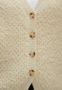 Beige strukturierte Strickjacke mit vier großen durchsichtigen braunen Knöpfen an der Front, Nahaufnahme des Knopfbereichs und des Stoffs.
