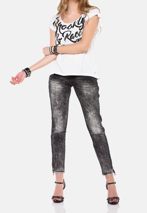 Witte korte mouwen t-shirt met zwarte letters, gecombineerd met zwart-grijze spijkerbroek met een versleten afwerking en ritsen bij de enkels.