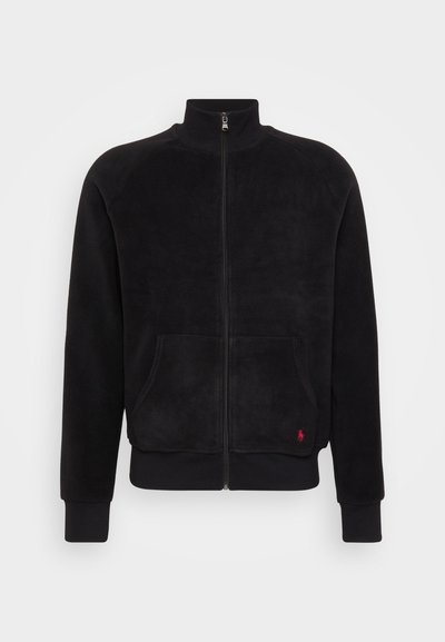 Svart fleecejakke med glidelås og høy krage, to frontlommer og ribbede mansjetter. Har en liten rød logo på venstre side.