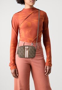 Brun mønstret taske med rektangulær form, der har en lys stribe og logo. Båret crossbody med en metal kædestrop.