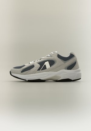 Baskets de sport grises et noires avec semelle blanche et design à lacets, avec un logo blanc sur le côté et des panneaux en tissu mesh.