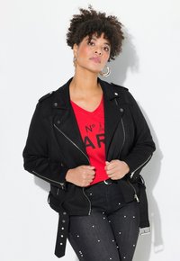 Black faux leather biker jacket with zip details, silver hardware, and a belted waist. Worn over a red graphic t-shirt and dark jeans with pearl accents.