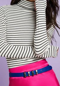 Gestreifter Rollkragenpullover in Weiß und Schwarz mit langen Ärmeln, kombiniert mit einem leuchtend pinken Satrock und einem blauen Gürtel mit schwarzen Akzenten.