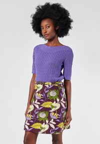 Purple cable-knit short-sleeve sweater with a wide neckline, paired with a purple floral print skirt featuring green and yellow accents and a belt.